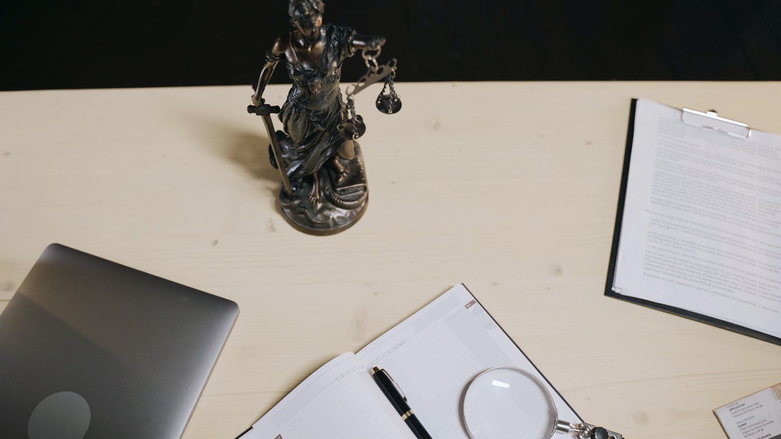 Legal documents and a Lady Justice statue on a light desk, seen from above