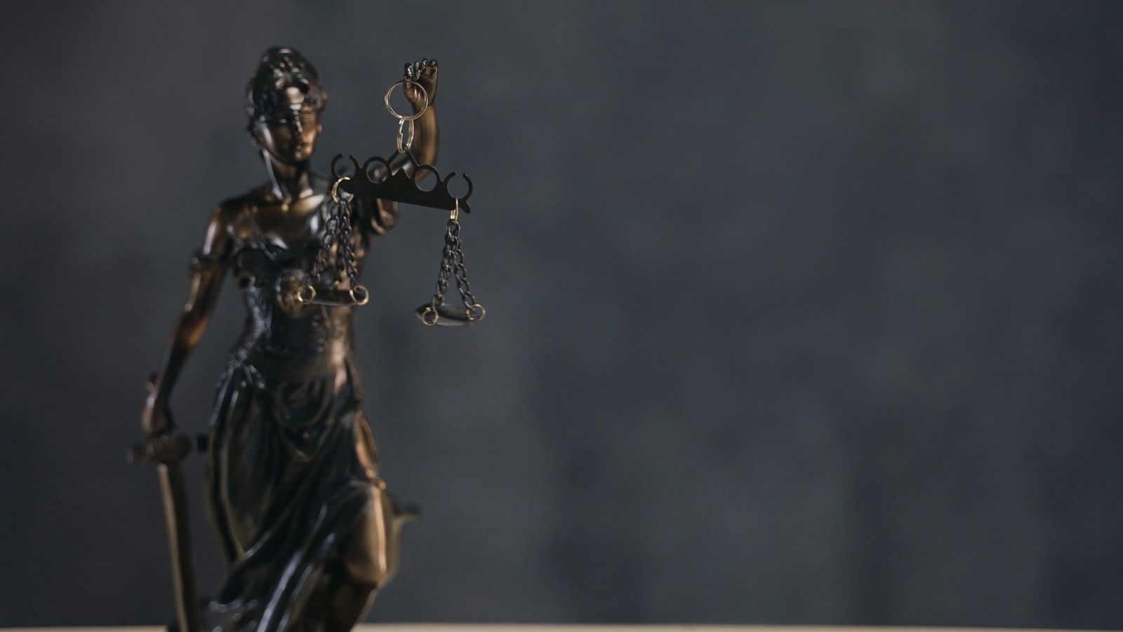 A bronze Lady Justice statue against a dark wall